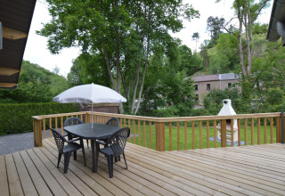 Wooden deck at Le Chalet Chaleureux A in Belgium with outdoor dining set, umbrella, and garden view.