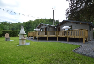 Außenansicht einer Glamping-Unterkunft mit Holzterrasse, Sonnenschirmen, Grillbereich und Rasenfläche.