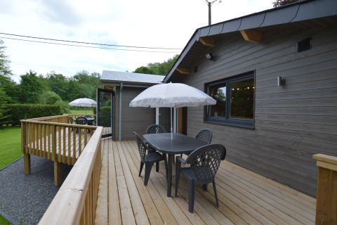 Wooden deck at Le Chalet Chaleureux A in Belgium featuring a patio set with umbrella and scenic views.