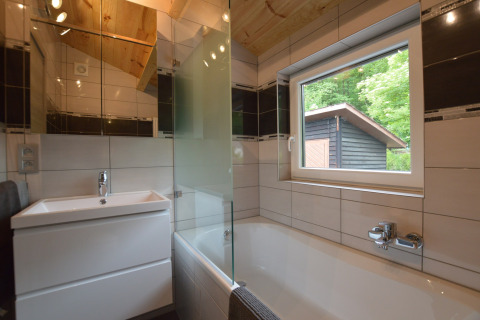 Modern bathroom at Le Chalet Chaleureux A, Belgium, featuring a bathtub, window, and wood ceiling.