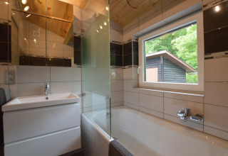 Modern bathroom at Le Chalet Chaleureux A, Belgium, featuring a bathtub, window, and wood ceiling.