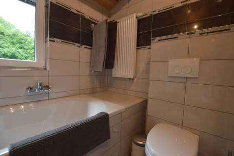 Modern bathroom in Le Chalet Chaleureux A, Belgium, featuring bathtub, toilet, towel rack and tiles.