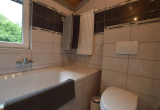 Modern bathroom in Le Chalet Chaleureux A, Belgium, featuring bathtub, toilet, towel rack and tiles.