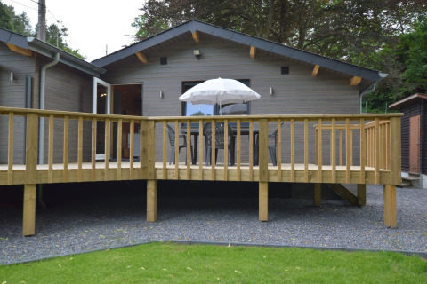 Wooden chalet with deck, outdoor table, chairs, and umbrella at Le Chalet Chaleureux A in Belgium.