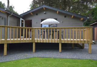 Wooden chalet with deck, outdoor table, chairs, and umbrella at Le Chalet Chaleureux A in Belgium.