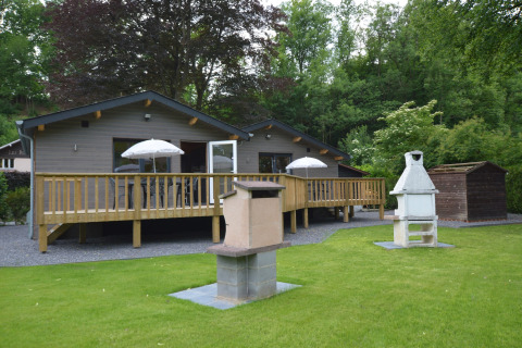 Outdoor view of Le Chalet Chaleureux A in Belgium with deck, lawn, patio umbrellas and barbecue spots.