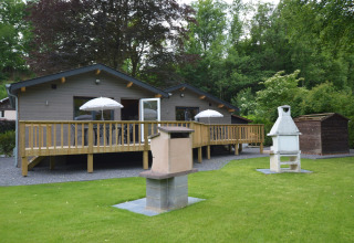 Outdoor view of Le Chalet Chaleureux A in Belgium with deck, lawn, patio umbrellas and barbecue spots.