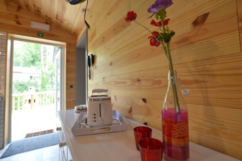 Cozy chalet hallway in wood, open door to terrace, toaster, glass bottle with flowers, red cups.