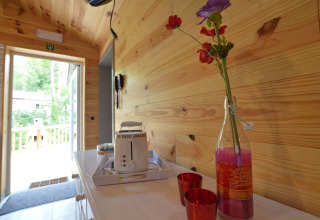 Cozy chalet hallway in wood, open door to terrace, toaster, glass bottle with flowers, red cups.