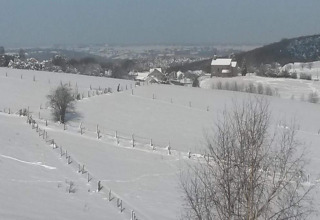 Snow-covered landscape with fences, trees and chalet 'Le Chalet Chaleureux A' in Belgium on a bright winter day.