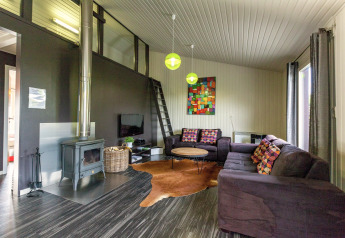 Soggiorno moderno nello Chalet «Orange» in Belgio con stufa a legna, divani scuri e cuscini colorati.