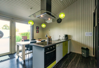 Cucina moderna al Chalet Orange in Belgio, con tavolo da pranzo, lampade verdi e ampia finestra.