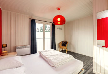 Camera luminosa allo Chalet Orange in Belgio con letto matrimoniale, sedia in vimini e lampada rossa.