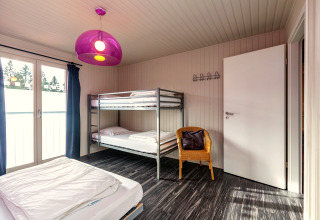 Camera nel Chalet «Orange» in Belgio con letto a castello, letto singolo, sedia in vimini e lampada viola.