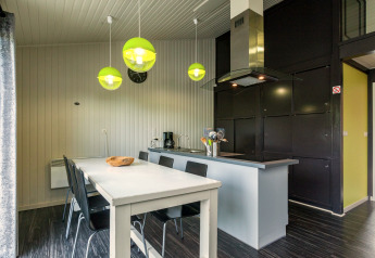 Zona pranzo e cucina moderna nello Chalet «Orange» in Belgio con lampade verdi e parete nera.