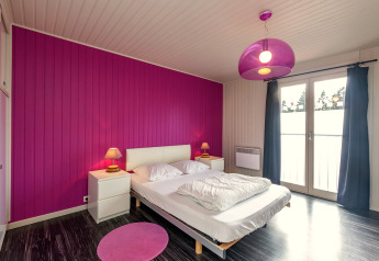 Camera moderna allo Chalet Orange in Belgio con parete rosa, letto matrimoniale e finestre ampie.