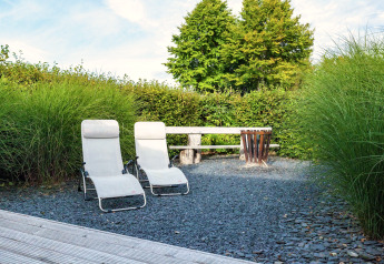 Area relax esterna presso Chalet «Orange» in Belgio con sedie a sdraio, panca e siepi verdi alte.