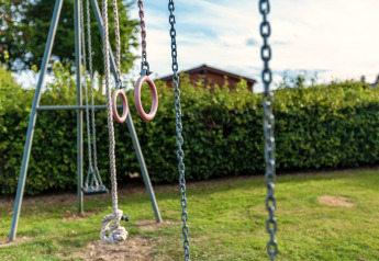 Parco giochi nel giardino dello Chalet Orange in Belgio, altalene, corde e anelli con siepe sullo sfondo.