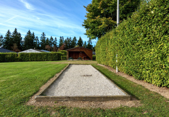 Campo di bocce in ghiaia presso Chalet Orange in Belgio, circondato da siepi e alberi verdi.