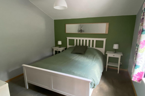 Slaapkamer in lodge «Le coeur du brâme» in België met groene muur, wit bed en nachtkastjes.