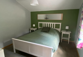 Slaapkamer in lodge «Le coeur du brâme» in België met groene muur, wit bed en nachtkastjes.