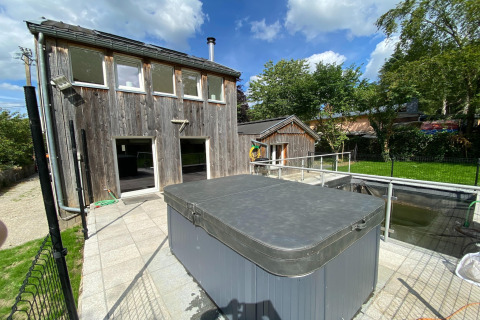 Buitenfoto van lodge 'Le coeur du brâme' in België, met houten gebouw, hottub en groene tuin.
