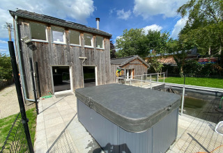 Buitenfoto van lodge 'Le coeur du brâme' in België, met houten gebouw, hottub en groene tuin.