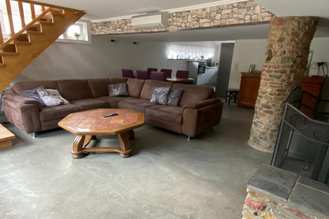 Woonkamer met bruine hoekbank, houten tafel en stenen pilaar in de lodge 'Le coeur du brâme' in België.