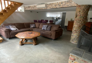 Woonkamer met bruine hoekbank, houten tafel en stenen pilaar in de lodge 'Le coeur du brâme' in België.