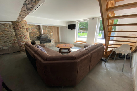 Gezellige woonkamer in Le coeur du brâme lodge in België met bankstel, houtkachel en grote ramen naar buiten.