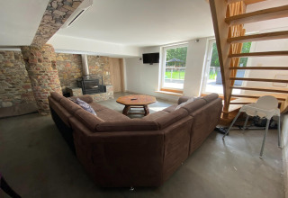 Gezellige woonkamer in Le coeur du brâme lodge in België met bankstel, houtkachel en grote ramen naar buiten.