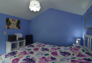 Slaapkamer in lodge ‘Le coeur du brâme’ in België met blauwe muren, bloemenbeddengoed en moderne inrichting.