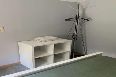 Hoek van een kamer in lodge 'Le coeur du brâme' in België met een klerenhanger en een wit rek met handdoeken.