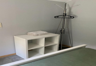 Hoek van een kamer in lodge 'Le coeur du brâme' in België met een klerenhanger en een wit rek met handdoeken.
