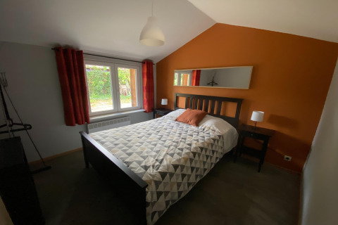 Slaapkamer in Le coeur du brâme lodge in België met oranje muur, tweepersoonsbed en groot raam.