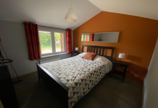 Slaapkamer in Le coeur du brâme lodge in België met oranje muur, tweepersoonsbed en groot raam.