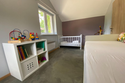 Kinderkamer bij lodge 'Le coeur du brâme' in België met speelgoed, kast, ledikant en grijze muren.