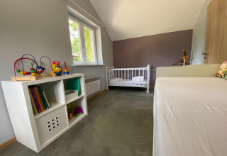Kinderkamer bij lodge 'Le coeur du brâme' in België met speelgoed, kast, ledikant en grijze muren.