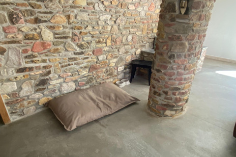 Stenen muur, bruin kussen en voerbakken op de vloer in lodge Le coeur du brâme in België, minimalistisch.