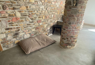 Stenen muur, bruin kussen en voerbakken op de vloer in lodge Le coeur du brâme in België, minimalistisch.
