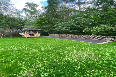 Groene tuin met houten prieeltje en hek bij de lodge Le coeur du brâme in België, omgeven door bos.