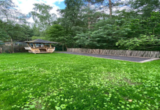 Groene tuin met houten prieeltje en hek bij de lodge Le coeur du brâme in België, omgeven door bos.
