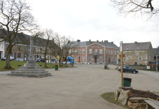 Rustig dorpsplein in België met een stenen monument, historische huizen en het gemeentehuis op de achtergrond.
