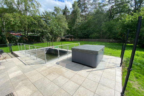 Buitenterras met overdekte jacuzzi en omheinde vijver in de tuin bij Le coeur du brâme lodge in België.