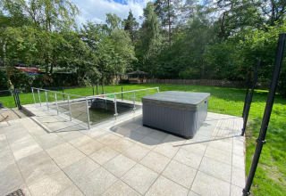 Buitenterras met overdekte jacuzzi en omheinde vijver in de tuin bij Le coeur du brâme lodge in België.