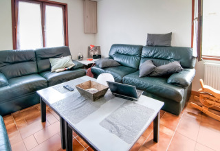 Bright lounge at Au Coeur du Pêcheur in Belgium with leather sofas, a coffee table, and large windows.