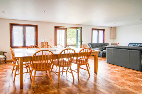 Dining and living area inside Au Coeur du Pêcheur lodge in Belgium with wooden chairs and tiled floor.