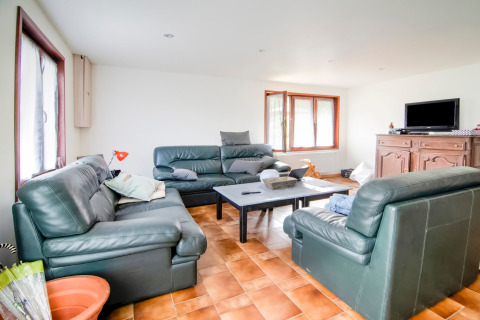 Living room with green leather sofas, coffee table, TV on wooden cabinet and large windows at a Belgian lodge.
