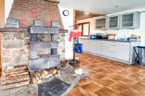 Rustic kitchen in Au Coeur du Pêcheur lodge, Belgium, with wood stove, stone hearth, and modern cabinets.