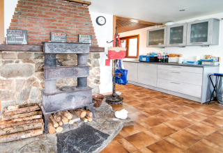 Rustic kitchen in Au Coeur du Pêcheur lodge, Belgium, with wood stove, stone hearth, and modern cabinets.